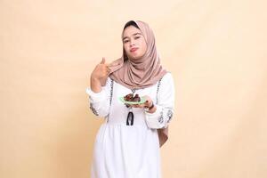 a beautiful Asian Muslim girl wearing a hijab pouting, pointing to the left and carrying dates for the sahur menu and breaking the fast. used for advertising, health, Eid and Ramadan photo