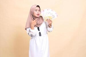 portrait of a beautiful indonesia Muslim woman wearing a hijab sullen and annoyed, holding and pointing to a gift or fitrah to the left on Eid day. used for advertising, giveaways, Eid and Ramadan photo