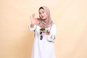 A beautiful Asian Muslim woman wearing a hijab smiled and took a date forward and brought some dates for sahur and breaking the fast. used for advertising, health, Eid and Ramadan photo