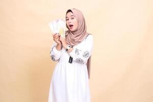 Portrait of a beautiful indonesia Muslim woman wearing a hijab looks up holding and showing off a gift or fitrah to the right on Eid day. used for advertising, giveaways, Eid and Ramadan photo