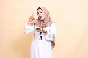 a beautiful indonesia Muslim woman wearing a hijab was surprised to point upwards and bring dates for the sahur menu and breaking the fast. used for advertising, health, Eid and Ramadan photo