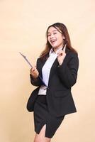 Beautiful formal indonesia executive mature woman in suit can idea stand and pose bring clipboard pen to camera, 3 by 4 body portrait on yellow background for commercial, vacancy and business photo