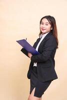 Beautiful formal Asian executive mature woman in suit smiling standing and taking notes pose taking clipboard to camera, 3 by 4 body portrait on yellow background for commercial, vacancy and business photo