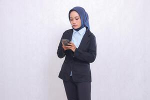 Asian office executive woman wearing a hijab stands elegantly operating her cellphone. Beautiful Muslim woman in blue shirt used for business, finance and technology content photo