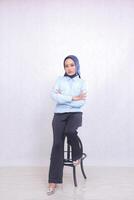 full body young Asian office woman wearing a hijab blue shirt sitting in an elegant chair with arms crossed. Beautiful Muslim women use business, finance and fashion content photo