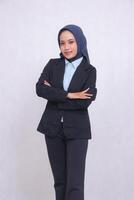 Portrait of an adult Asian blue shirt office woman wearing a hijab, standing at right angles, smiling elegantly, arms crossed. Beautiful Muslim women use business, technology and fashion content photo