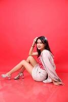 Sexy Asian Indonesian woman smiling facing left wearing a red patterned tank top and cream formal blazer, hands holding thighs photo