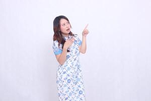 Beautiful shocked Javanese Chinese woman wearing a modern Chinese dress glances and all hands point to the top left on a white background. happy Chinese New Year photo