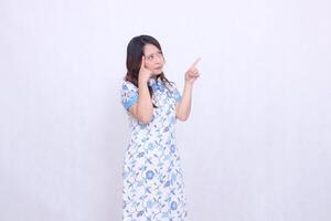 beautiful Javanese Chinese woman thinking wearing a modern Chinese dress showing her brain and hand pointing up left on a white background. happy Chinese New Year photo