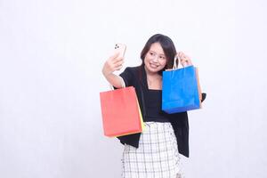 woman customer 20s smiling happily while taking photo in front of cellphone up hand showing order bringing shopping paper bag in the middle isolated on white background