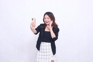 Beautiful Indonesian office woman in her 20s with a cheerful expression looking at her cream colored cellphone gadget while making a call for a promo isolated on a white background photo