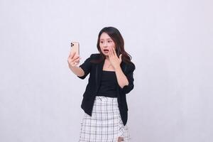 beautiful Indonesian office woman in her 20s with a shocked expression looking at her cream colored cellphone gadget while making a call for a promo isolated on a white background photo