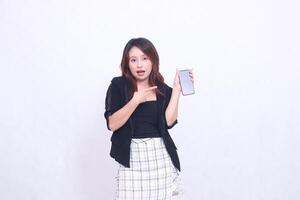 beautiful Indonesian office woman 20s expression of surprise on promotion of cellphone gadget screen for promo while pointing at it underneath isolated white background photo
