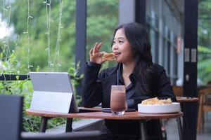 the elegance of a young Asian woman in a candid online meeting snacking in front of a laptop in a cafe photo