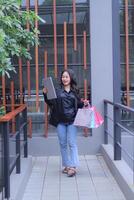 young Indonesian girl is happy to get a special price for online orders, walking candidly bringing a paper bag and laptop computer, to promote online content, lifestyle, catalogs photo