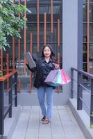 young Indonesian office girl is happy to get a discount price for an online order, walking candidly carrying a paper bag and laptop computer, to promote online content, lifestyle, catalogs photo