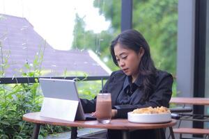 Beautiful Asian woman in office clothes is doing assignments in a cafe while enjoying food and drinks photo