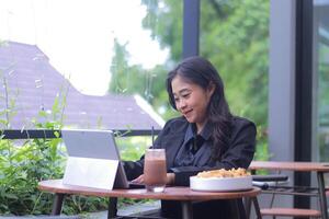 Beautiful smiling Asian woman in office clothes is doing assignments in a cafe while enjoying food and drinks photo