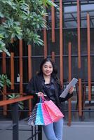 portrait of young asian woman manager smiling at camera online shopping, standing sender fence carrying paperbag and laptop computer, used for promotion to create online content photo