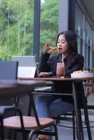 The elegance of a young Asian woman in an office meeting online while doing work by snacking on a laptop in a cafe photo