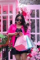 charm of beautiful asian woman in pink shirt happy cheating her friend hands carrying debit card, smartphone and paperbag in outdoor cafe for promotion of fashion, lifestyle, catalog photo