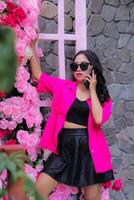 Beauty Asian woman in pink shirt wearing elegant glasses calling someone via cellphone holding flowers for fashion, lifestyle, banner, promo content photo