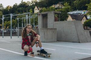 Teen girl skater with a skateboard is sitting and resting in the skaters park photo