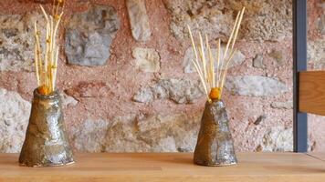 A unique design features a rustic vase on a wooden shelf set against a stone wall video