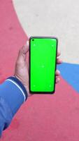 A man in an urban setting holds a smartphone with a green screen, showcasing modern technology video