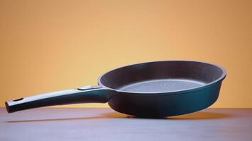 Black frying pan on an orange background. ACTION. Frying pan advertisement on a plain background. A spinning frying pan on a red background. video