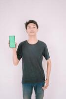 A Southeast Asian man holding a greenscreen phone, ready for customization. Perfect for adding your own content or app interface in a marketing or promotional context photo