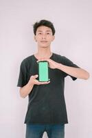 A Southeast Asian man holding a greenscreen phone. Perfect for adding custom content, app interfaces, or marketing messages, showcasing technology use in a versatile context. photo