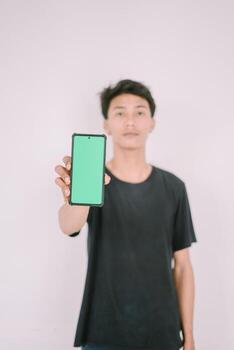 A Southeast Asian man holding a greenscreen phone. Perfect for adding custom content, app interfaces, or marketing messages, showcasing technology use in a versatile context. photo
