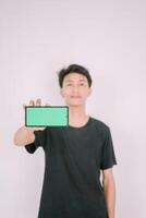 A Southeast Asian man holding a greenscreen phone, ready for customization. Perfect for adding your own content or app interface in a marketing or promotional context photo