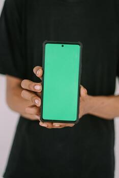 A Southeast Asian man holding a greenscreen phone. Perfect for adding custom content, app interfaces, or marketing messages, showcasing technology use in a versatile context. photo