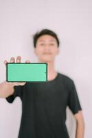 A Southeast Asian man holding a greenscreen phone, ready for customization. Perfect for adding your own content or app interface in a marketing or promotional context photo