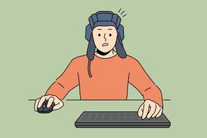 Man gamer plays tanks on computer, sitting at table with keyboard and wears tanker helmet vector