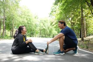Asian young woman in sportwear is Cramping her leg and boyfriend helping for relaxation of resilient and Muscle contraction after excersice and running in the Garden. Healthy on holiday Concept photo
