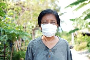 Asian old lady gardener is sweating and wearing glasses with white cloth mask for prevent the Covid-19 or Corona virus in Thailand and protect for Air Pollution Value Pm 2.5. Health elderly Concept. photo