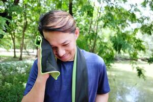 Young Asian sportman ralaxing and taking the fabric wiping sweat on the face on the face after exercise and running or jogging in the garden. photo