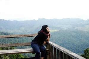 Asian woman sitting and relaxing on wooden bench on terrace for freedom journey with valley mountain and foggy in natural and travel destination in tropical rain forest photo