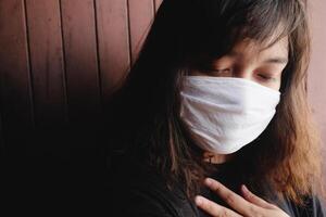 Asian Thai woman wearing a white cloth mask for prevent the Covid-19 or Corona virus and Air Pollution Value Pm 2.5 in Thailand. She is suffocating in Respiratory system. Health and illness concept photo
