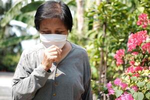 Asian old woman wearing a white cloth mask for prevent the Covid-19 or Corona virus and coughing in Thailand and protection for Air Pollution Value Pm 2.5. Health and medicine of elderly conconcept photo