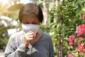 Asian old woman wearing a white cloth mask for prevent the Covid-19 or Corona virus and coughing in Thailand and protection for Air Pollution Value Pm 2.5. Health and medicine of elderly conconcept photo
