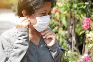 Asian old woman wearing a white cloth mask for prevent the Covid-19 or Corona virus in Thailand and protection for Air Pollution Value Pm 2.5. Health and medicine of elderly in garden concept photo