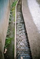 A stream of household runoff flows beneath, shielded by sturdy iron supports to prevent accidental slips, blending utility with safety photo