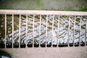 A stream of household runoff flows beneath, shielded by sturdy iron supports to prevent accidental slips, blending utility with safety photo