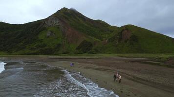 Top view of people by sea with mountain view. Clip. Coast with walking people and amazing mountains on cloudy day. Walk on mountain coast of ocean on cloudy day photo