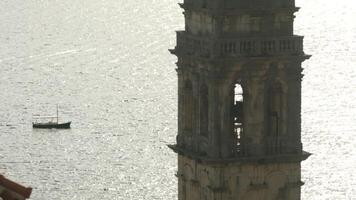 Large monuments standing next to the sea.Creative.A large stone tower and bell tower standing next to the sea with a small sail. video