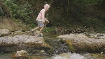 Side view of a boy jumping over the mountainous water stream. Creative. Forest lake and a boy having fun. video